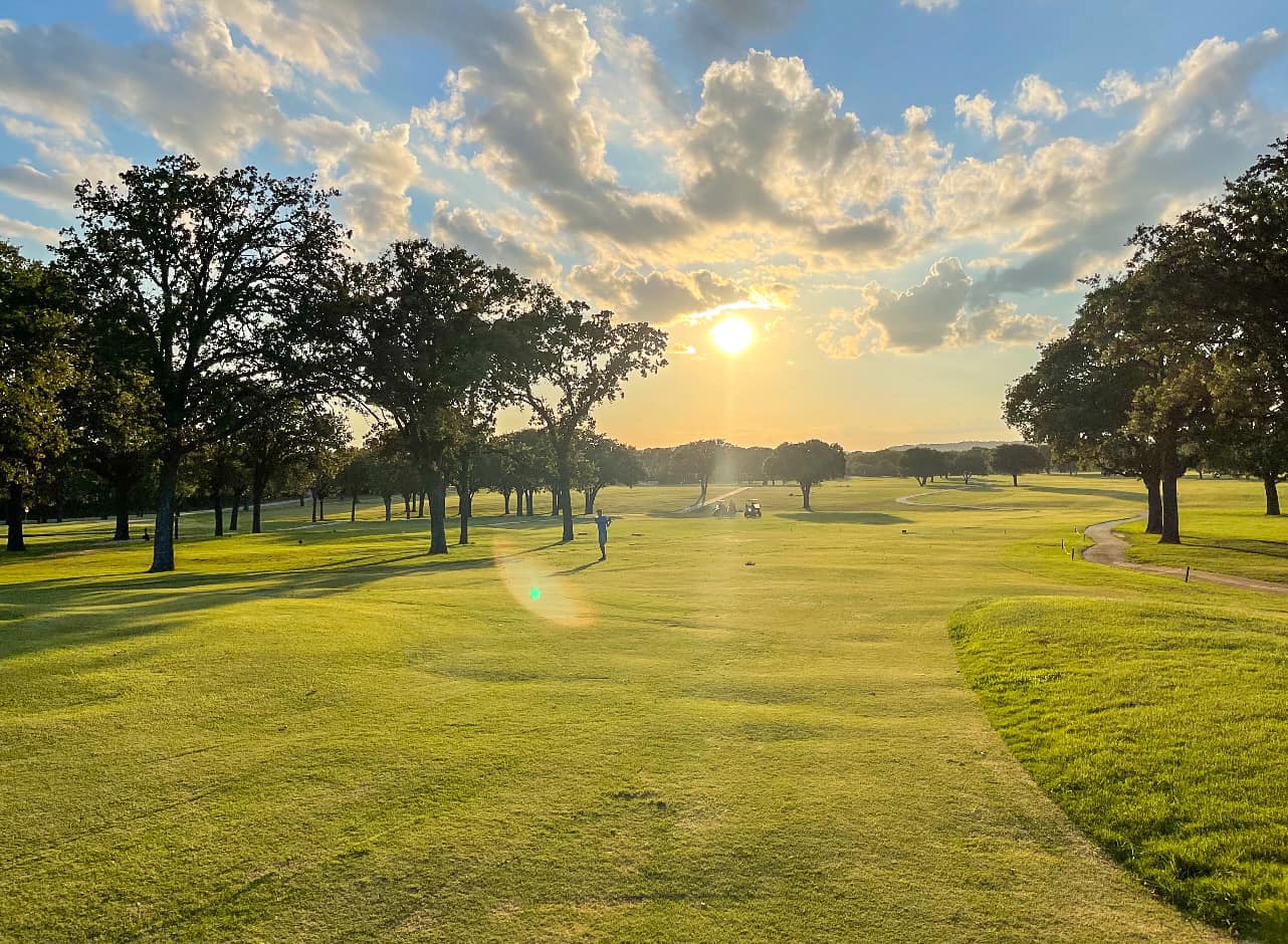 top of lake golf course hole shot with trees and a golfer playing on the green